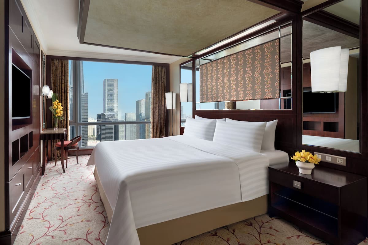 Habitación de hotel con una cama grande, un escritorio con silla, televisor y vistas a la silueta urbana.