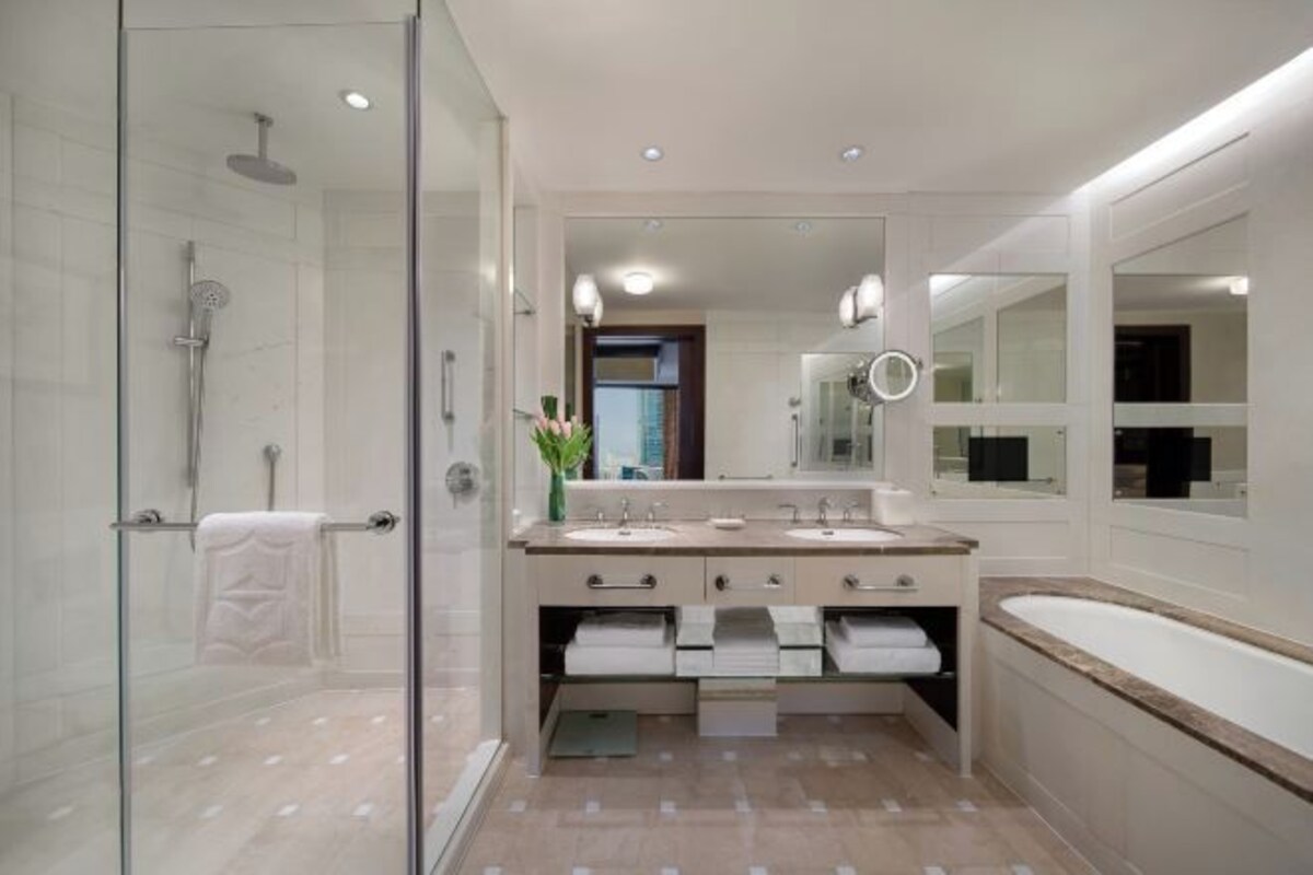 A modern bathroom with a glass shower enclosure, two sinks, a large mirror, and a bathtub.