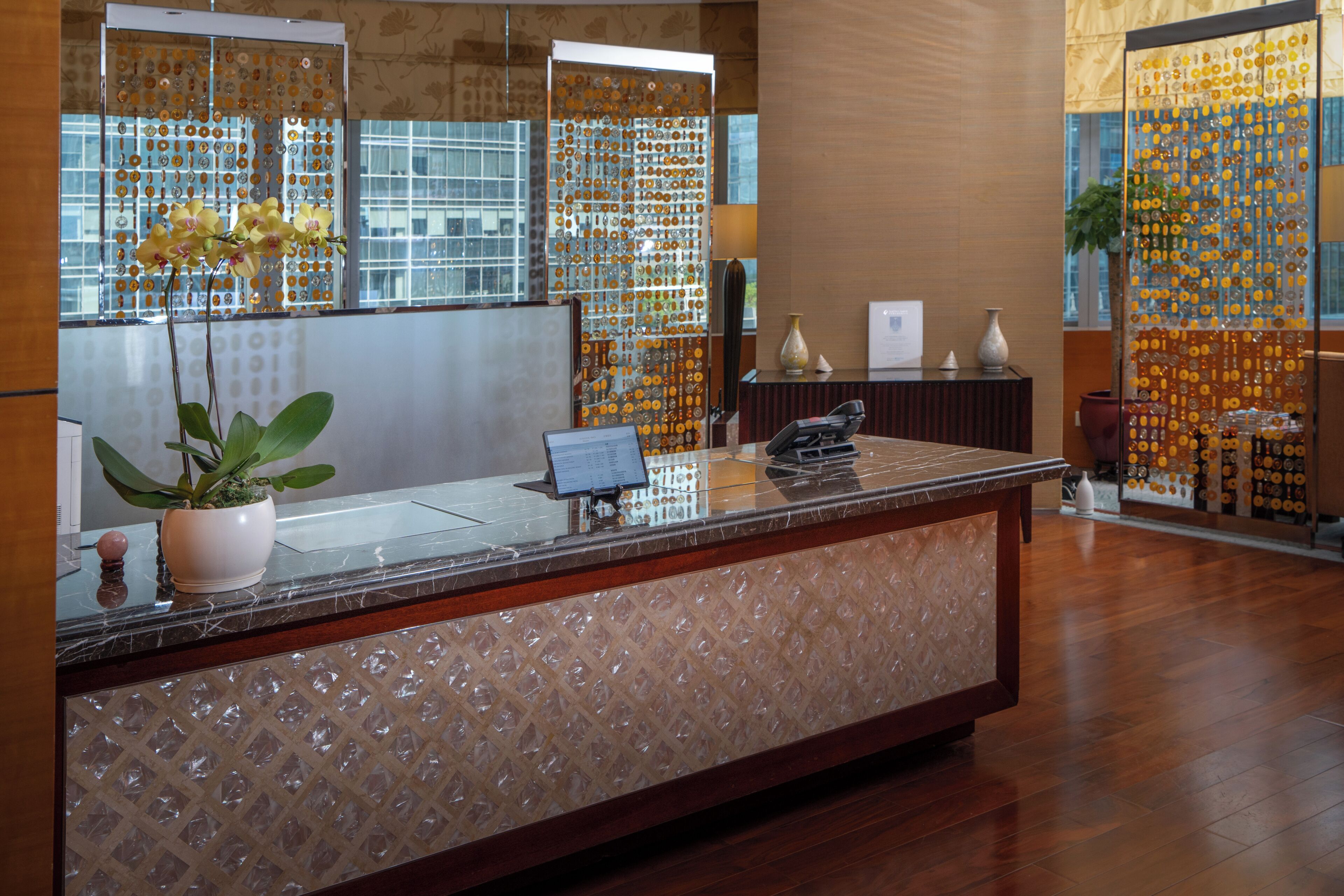 A reception desk with a potted plant, a computer, and decorative glass panels.