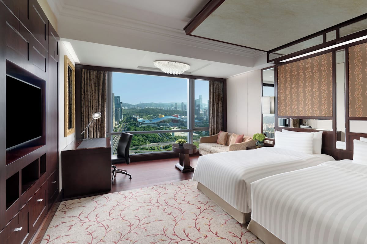 Habitación de hotel con una cama grande, un escritorio con una silla, televisión y vistas a la ciudad.