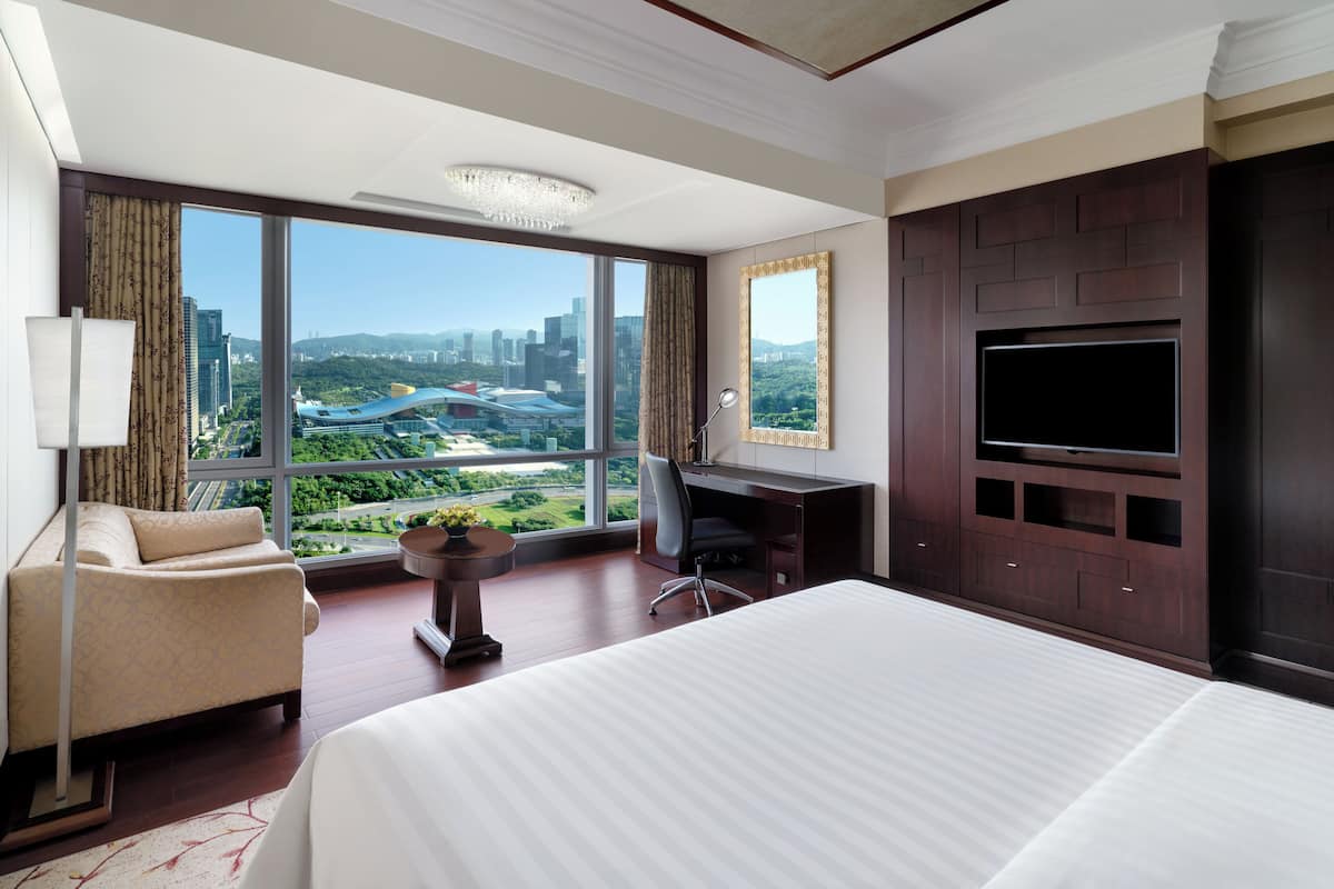 Habitación de hotel con una cama grande, un escritorio, una silla, un televisor y vistas a la ciudad.