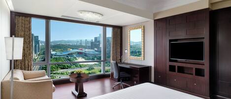 A hotel room with a large bed, a desk, a chair, a TV, and a view of the cityscape.