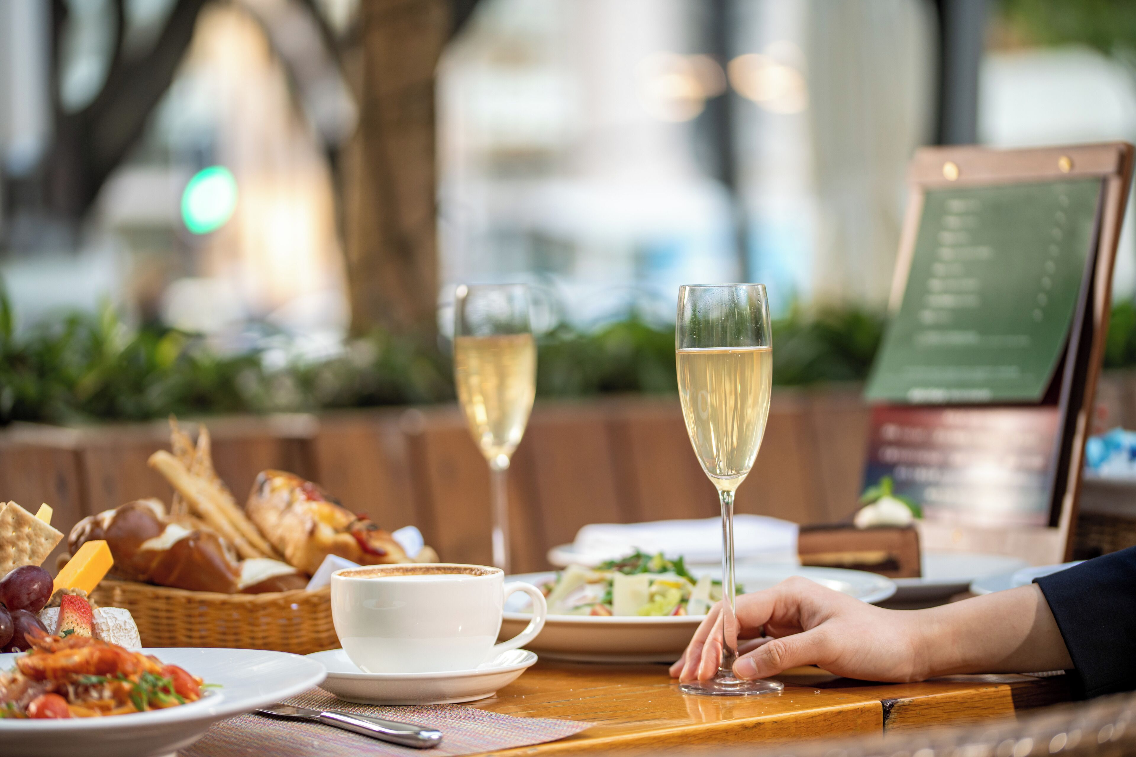 A dining table with a menu, a plate of food, a cup of coffee, and two glasses of wine.