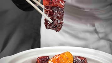 A person holding a piece of food with chopsticks over a plate of food.