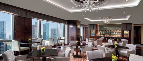 A spacious hotel lobby with a high ceiling, a grand chandelier, and a view of the city skyline.