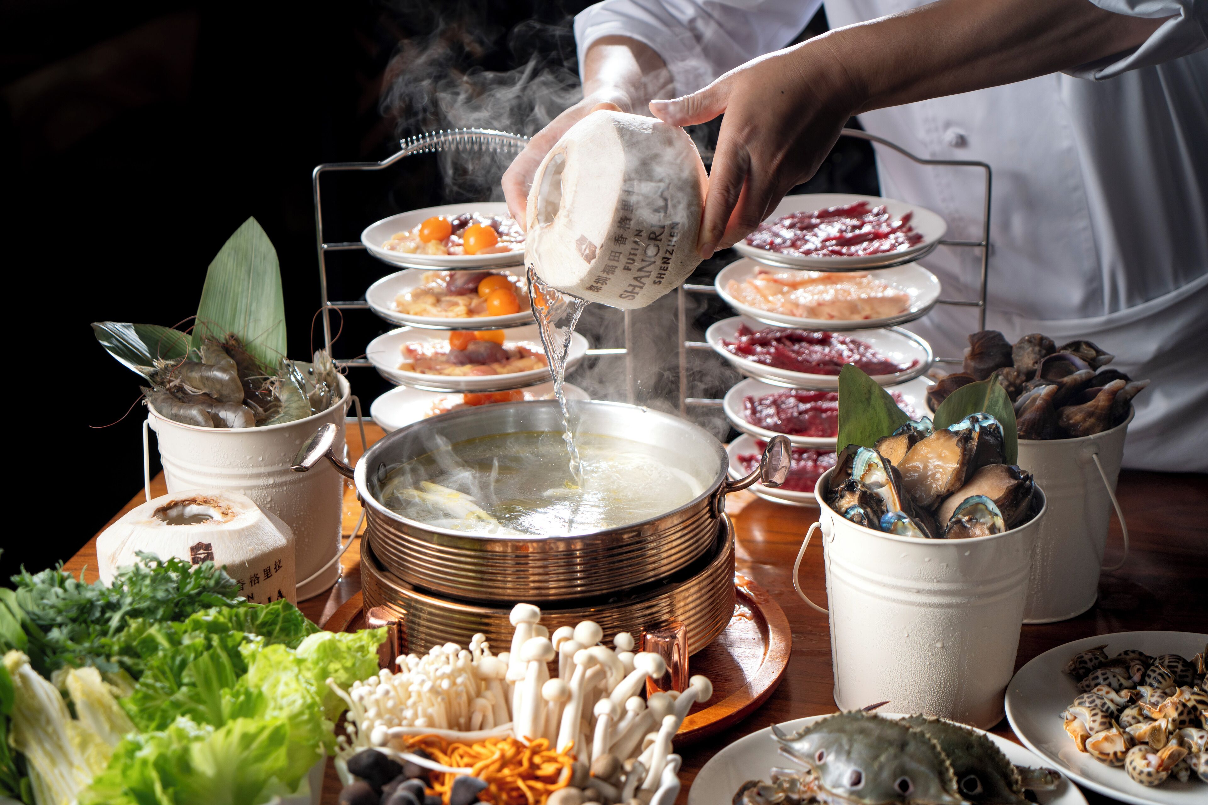 Un chef sirviendo líquido en una olla, rodeado de diversos platos e ingredientes.