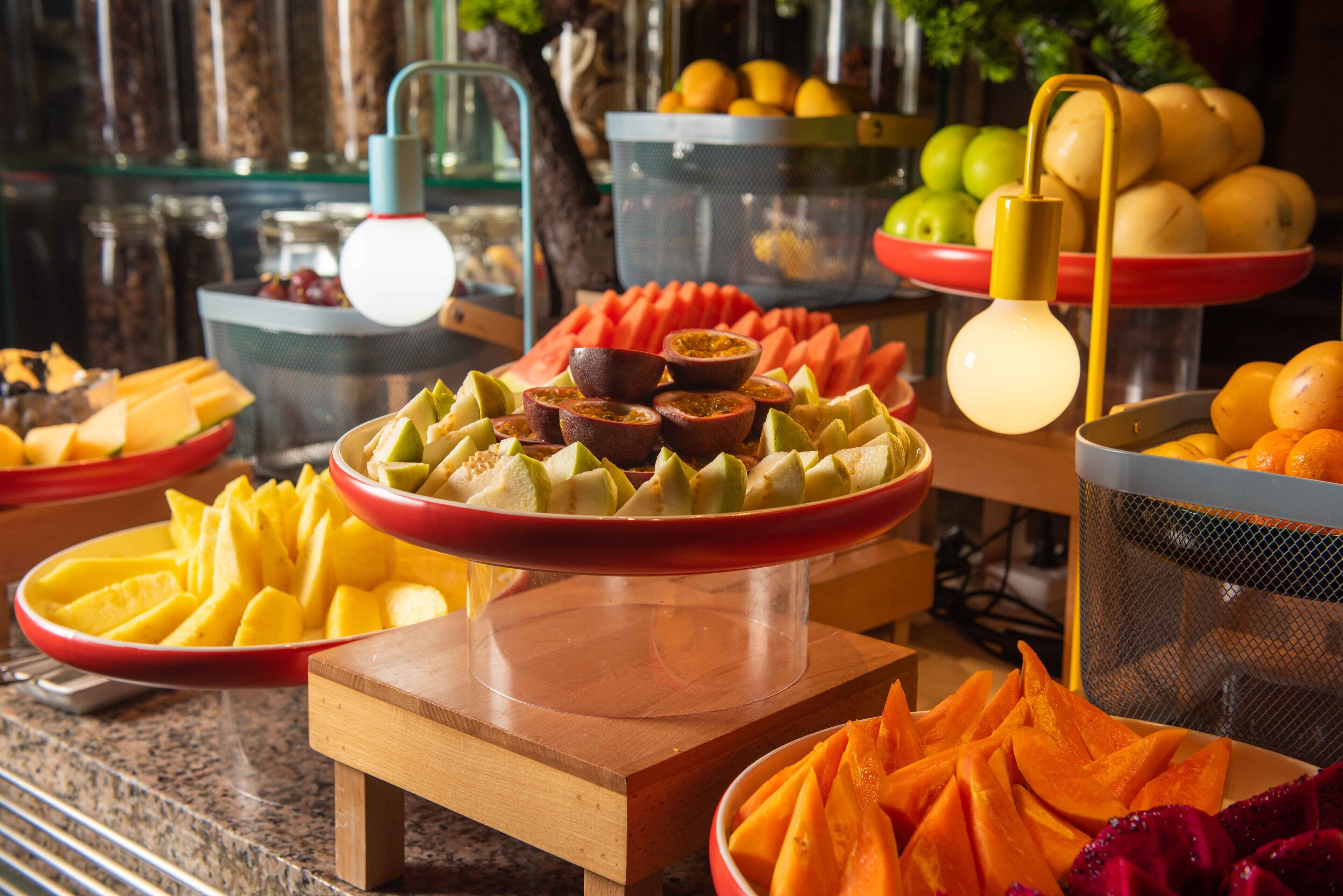 En buffet med et udvalg af frugter og grøntsager, heriblandt vandmelon, cantaloupe og appelsiner.