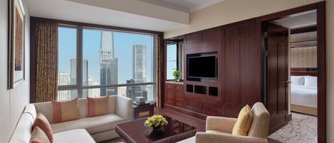 Una habitación de hotel moderna con un ventanal que ofrece vistas a la ciudad, un televisor de pantalla plana montado en un panel de madera, un sofá, una silla y una mesa de centro con un arreglo floral.