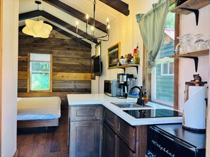 Una cocina compacta con cama empotrada, paredes de madera, lámpara colgante y ventana con persianas.