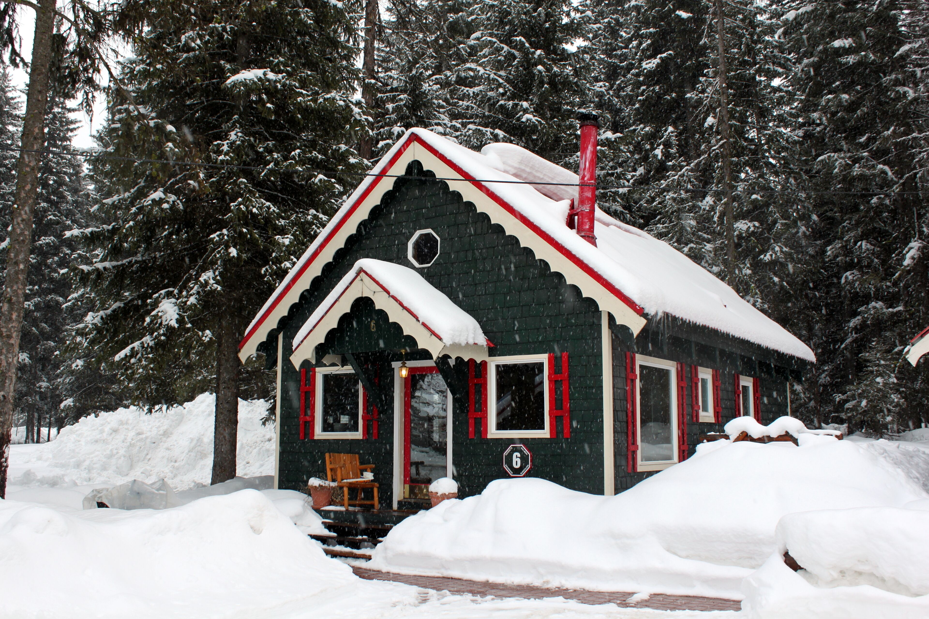 Une cabane enneigée, dotée d’une cheminée, entourée d’arbres.