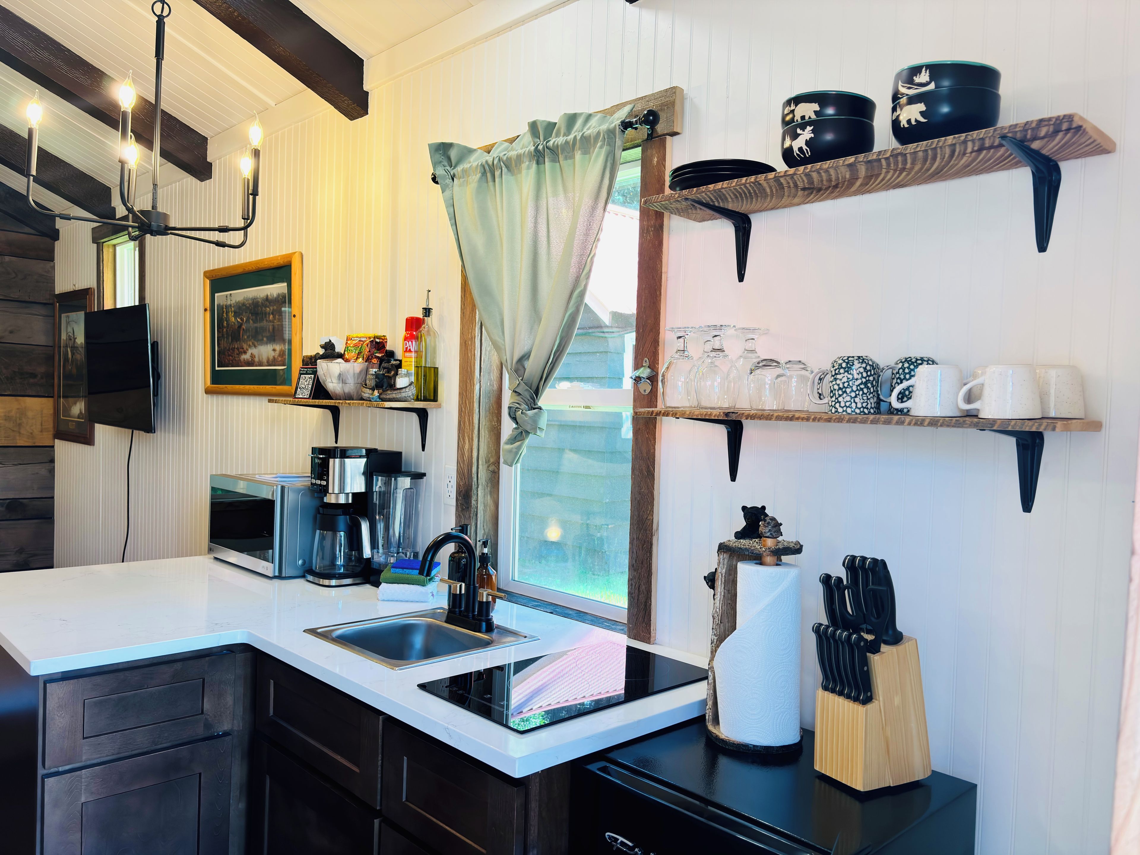 A kitchen with a sink, coffee maker, blender, and a window with curtains.