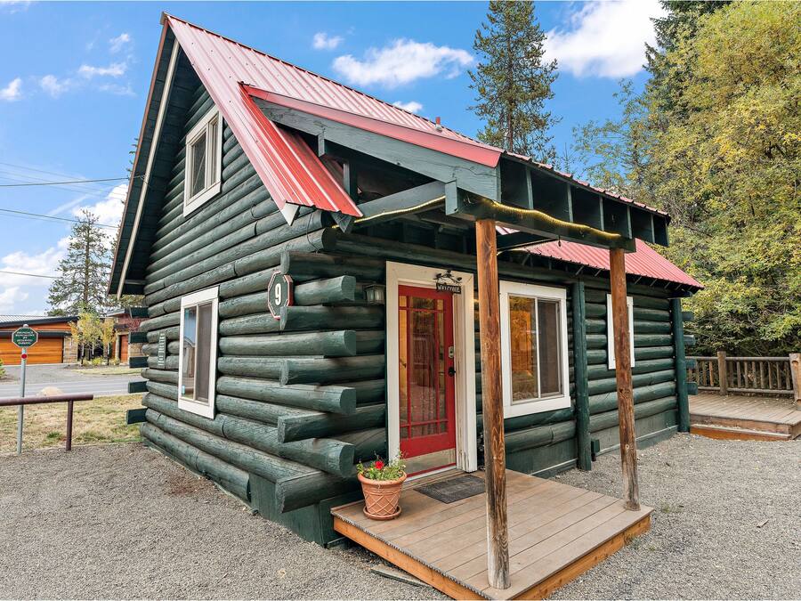 A log cabin with a red door, a porch, and a welcome sign.