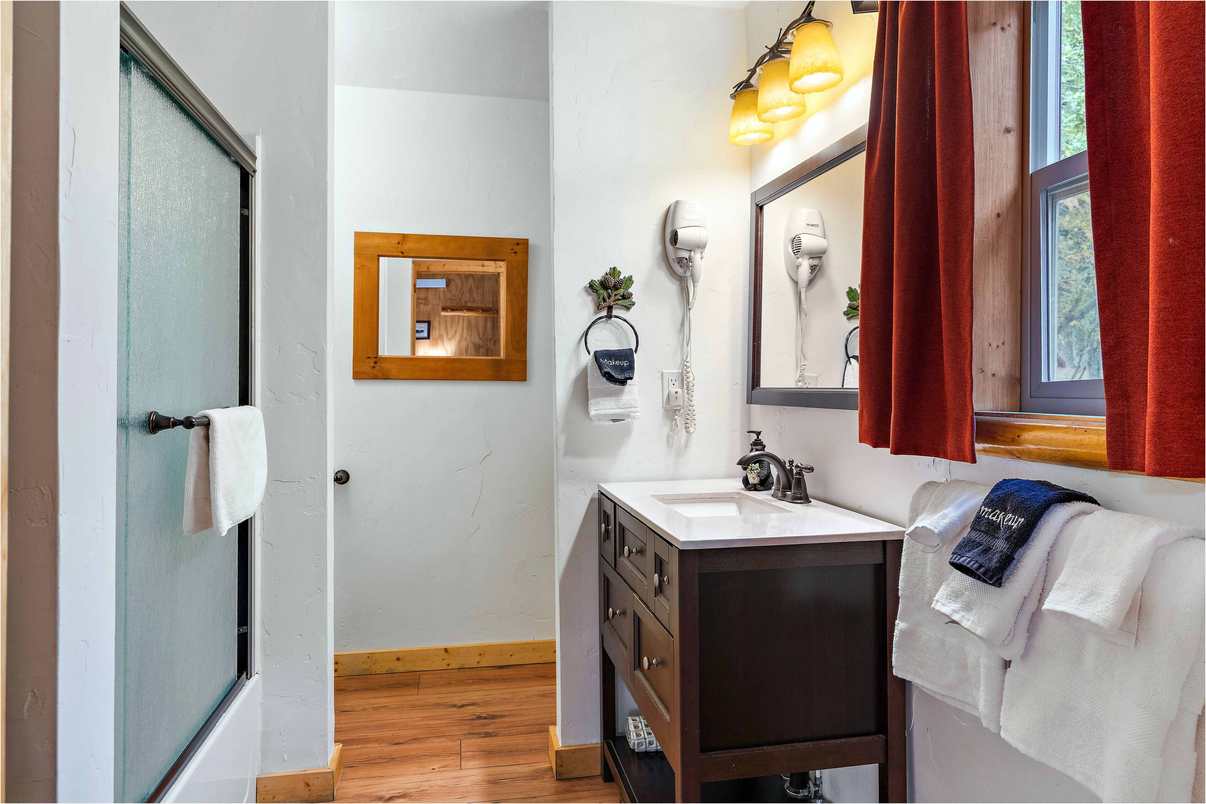 A bathroom with a wooden floor, a white sink, a mirror, a hairdryer, and a towel hanging on the wall.