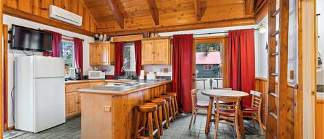A wooden cabin kitchen with a central island, bar stools, a refrigerator, and a dining table with chairs.