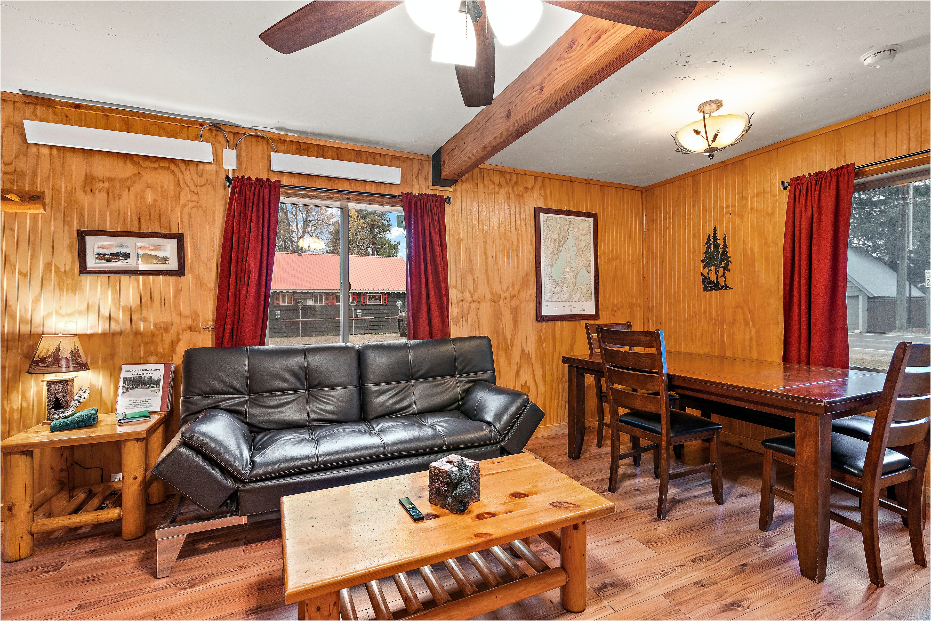 A cozy room with a wooden interior, a black leather sofa, a wooden dining table with chairs, and a wooden coffee table.
