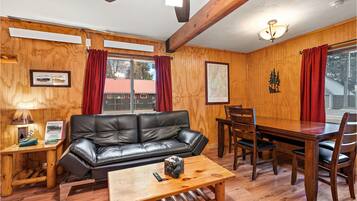 Una habitación acogedora con detalles de madera, un sofá de cuero negro, una mesa de comedor de madera con sillas y una mesa de centro de madera.