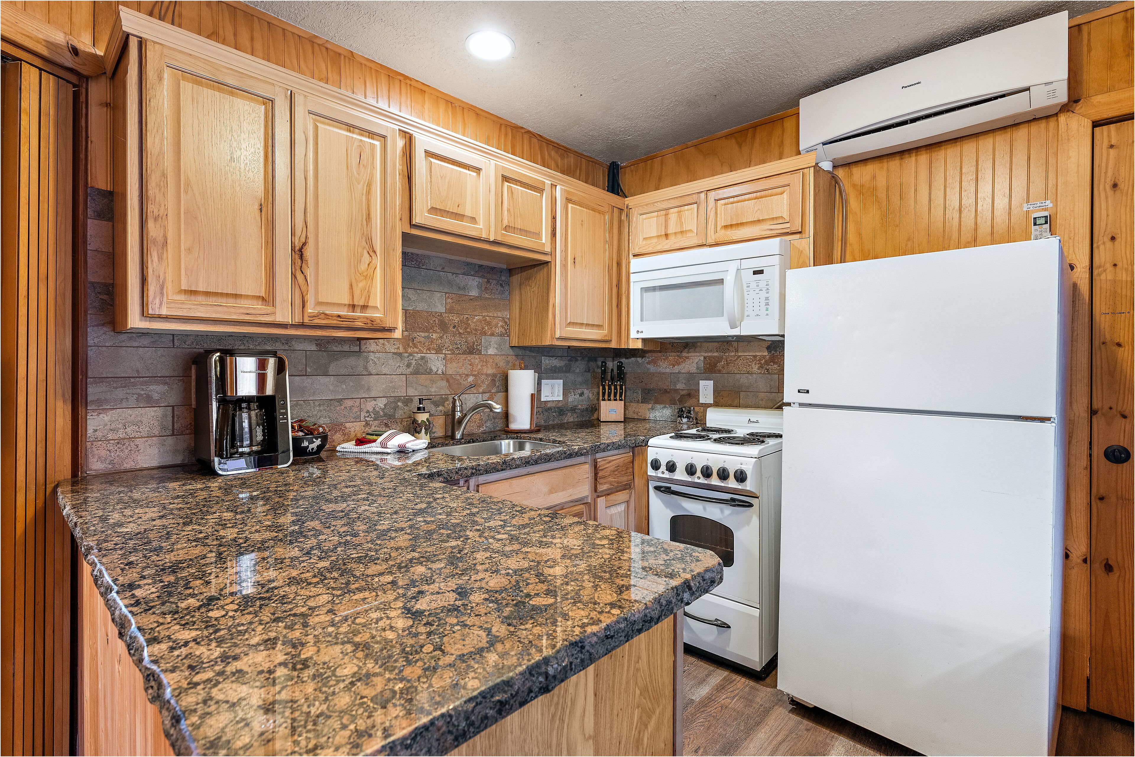 A kitchen with wooden cabinets, granite countertops, a microwave, a refrigerator, and a stove.