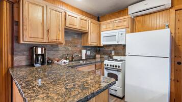 A kitchen with wooden cabinets, granite countertops, a microwave, a refrigerator, and a stove.