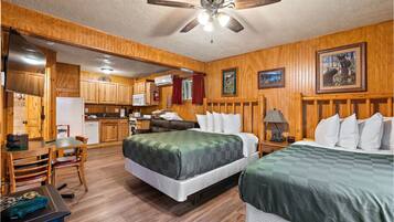 A room with two beds, a kitchenette, and a ceiling fan.