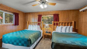 A room with two beds, wooden walls, a ceiling fan, and a window with curtains.