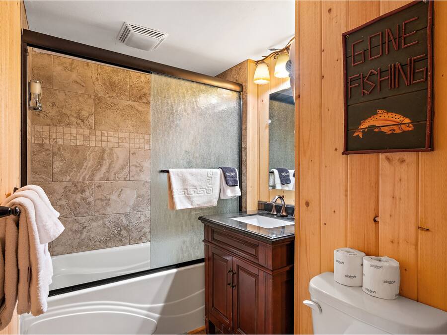 A bathroom with a bathtub, a sink, and a toilet. There is a towel rack with towels, a shower curtain, and a sign that says "Gone Fishing".