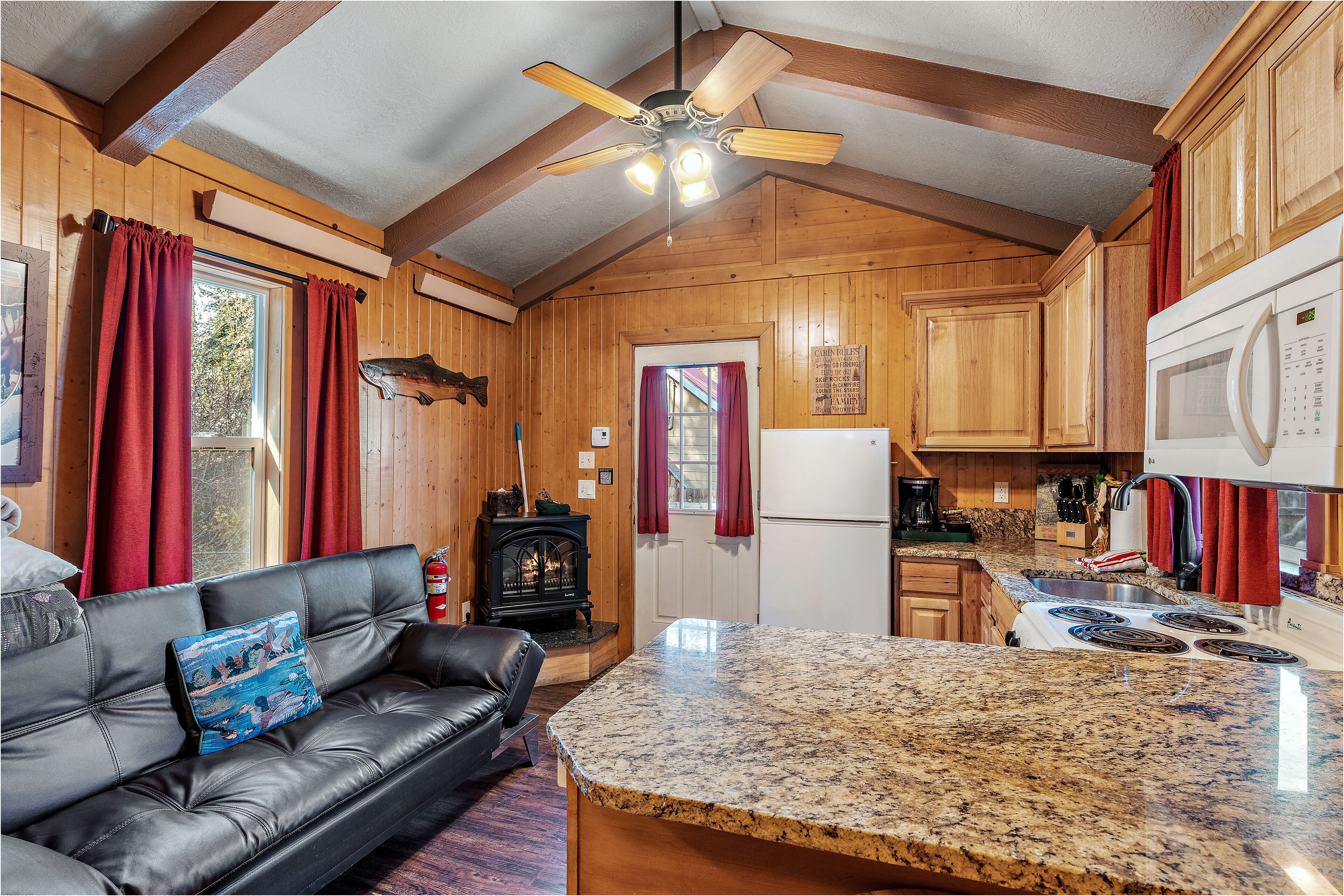 A cozy cabin interior with a fireplace, a kitchen with granite countertops, and a leather sofa with a decorative pillow.