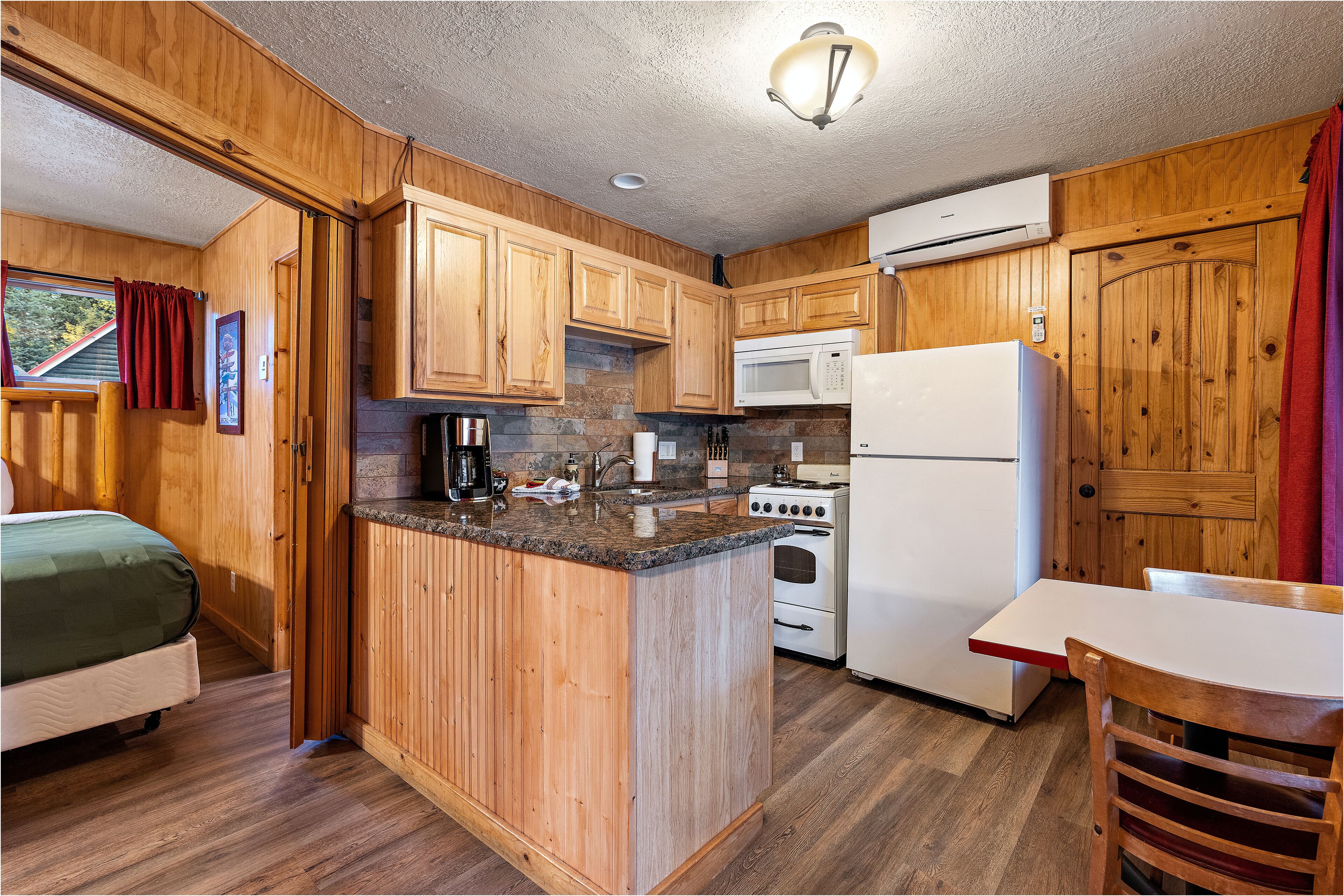 A compact kitchen with wooden cabinets, a granite countertop, a microwave, a stove, and a refrigerator.