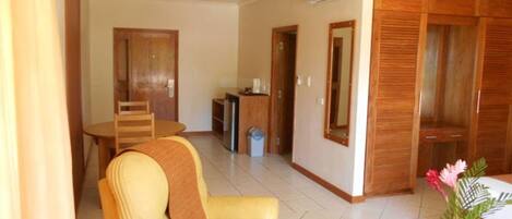 A room with a dining table, a chair, a small kitchenette, and a wardrobe.