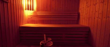 A sauna with wooden benches and a single bucket on the floor.