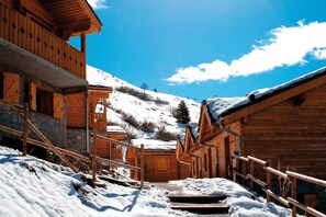A wooden cabin with a balcony, a stone staircase, and a snow-covered mountain in the background. - Résidence Lagrange Vacances Le Grand Panorama II (Valmeinier)