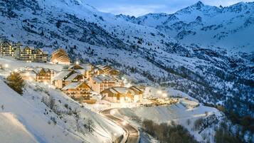 Bergresort bedekt met sneeuw, met meerdere chalets, een kronkelende weg en een skilift op de achtergrond.