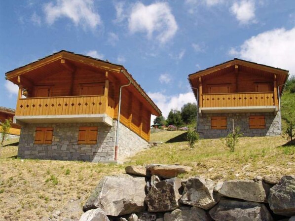 Two wooden cabins with stone foundations, wooden balconies, and wooden shutters. - Résidence Lagrange Vacances Le Grand Panorama II (Valmeinier)