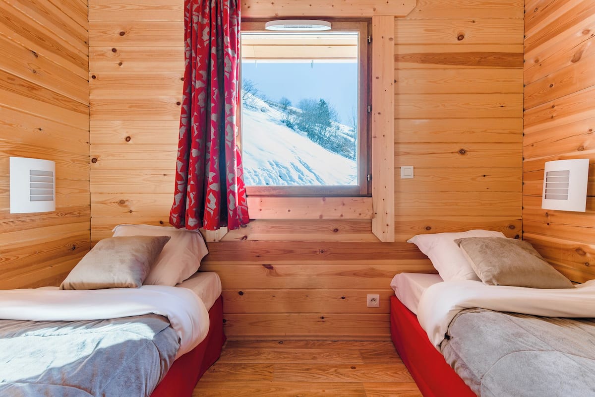 A cabin with two beds, a window with a view of a snowy landscape, and wooden walls.