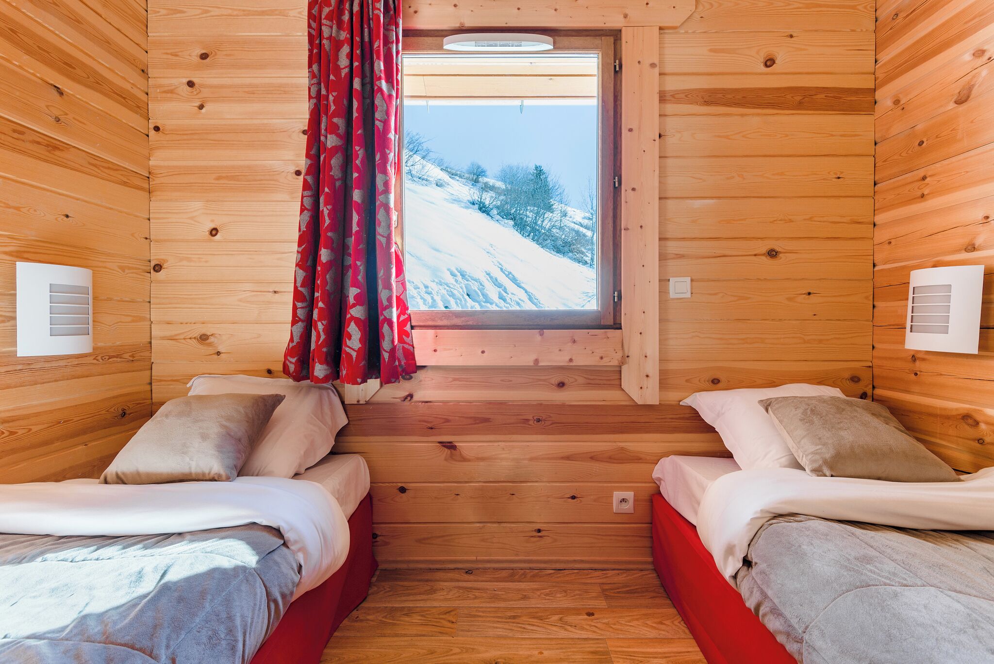 Uma cabana com duas camas, uma janela com vista para uma paisagem nevada e paredes de madeira.