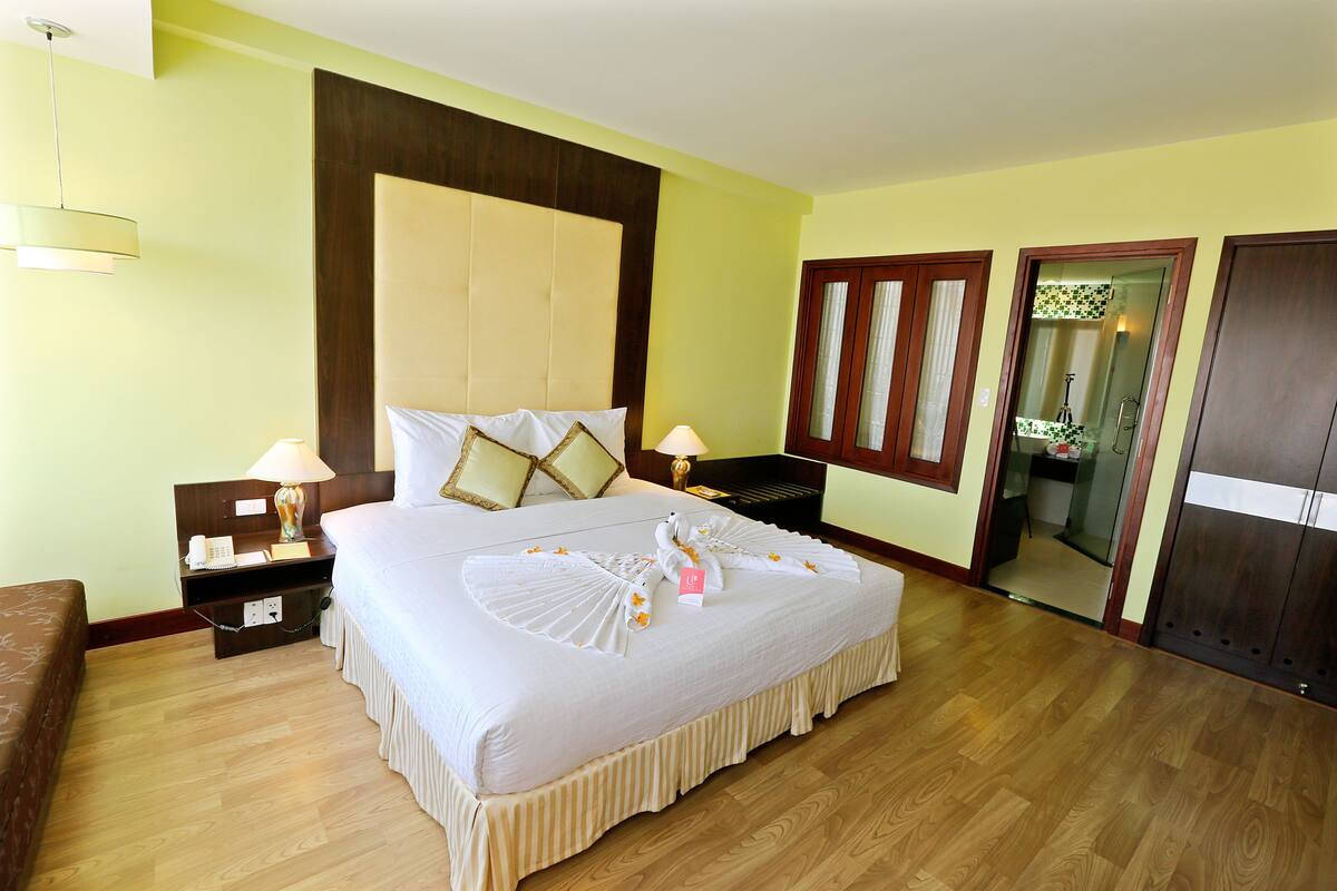 A hotel room with a large bed, wooden floor, and a mirror cabinet.