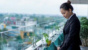 Eine Person deckt einen Tisch mit grünen Servietten und weißen Tellern auf einem Balkon mit Blick auf die Stadt.