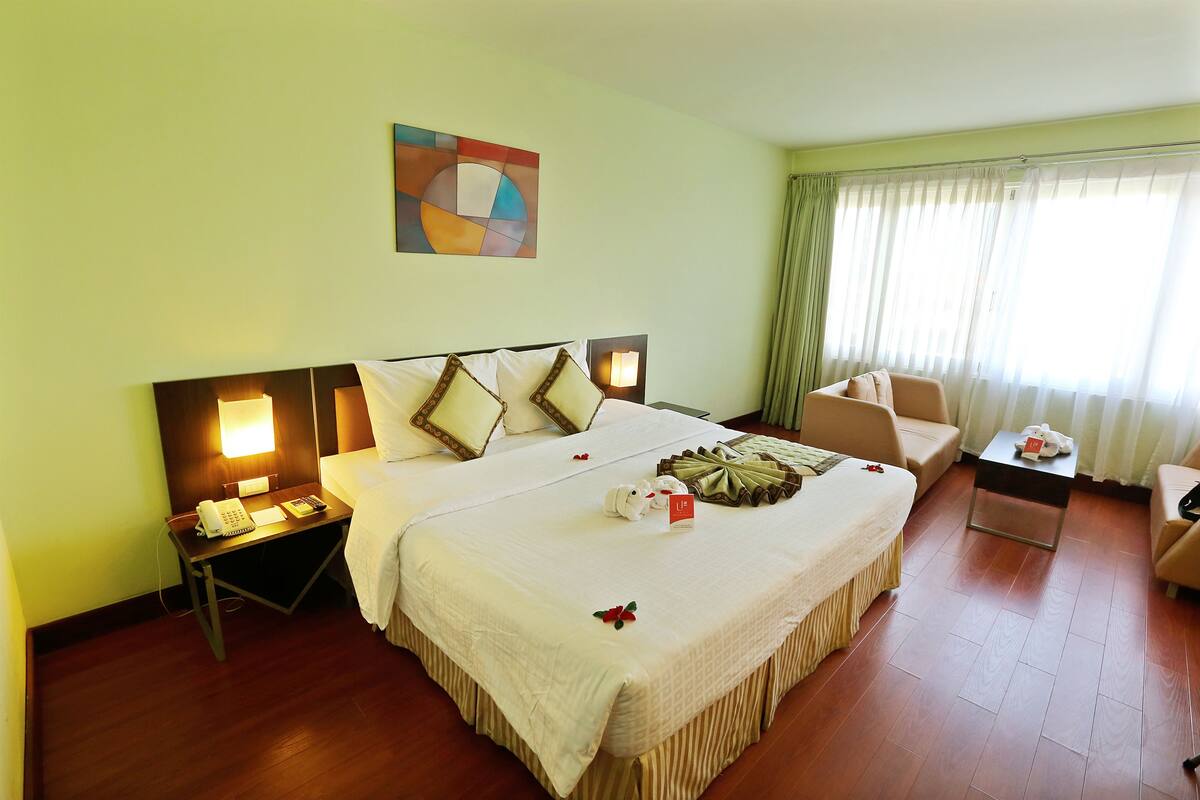 A hotel room with a large bed, bedside tables, a desk, a chair, and a view of the outside through the window.