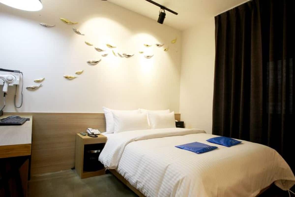 Ein Hotelzimmer mit einem Bett, einem Schreibtisch mit Telefon und einer Wandklimaanlage.