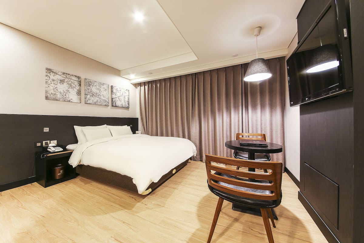 Ein Hotelzimmer mit Bett, Schreibtisch, Stuhl, Fernseher und Wandbildern.