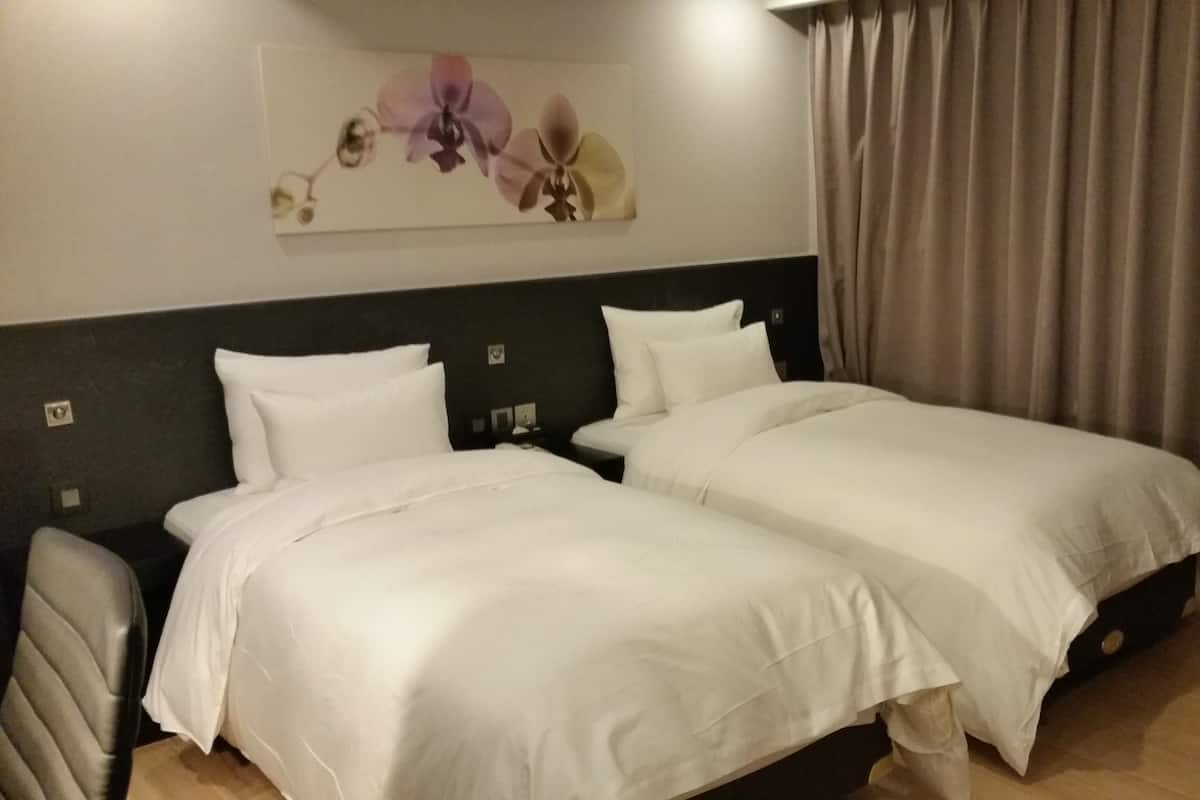 Ein Hotelzimmer mit zwei Einzelbetten, einem Kopfteil mit floralem Kunstwerk, einem Nachttisch und einem Vorhang.