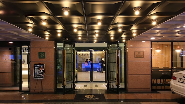 A hotel entrance with a modern design, featuring a reception desk, a signboard, and a car parked outside. - Hotel Kobos (Seoul)