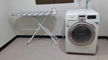 Un espacio pequeño para la ropa con lavadora blanca y una plancha.