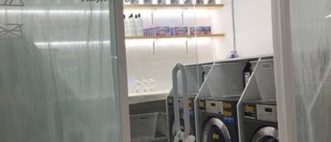 A modern laundry room with a glass partition, a washing machine, a dryer, and neatly arranged laundry supplies on shelves.