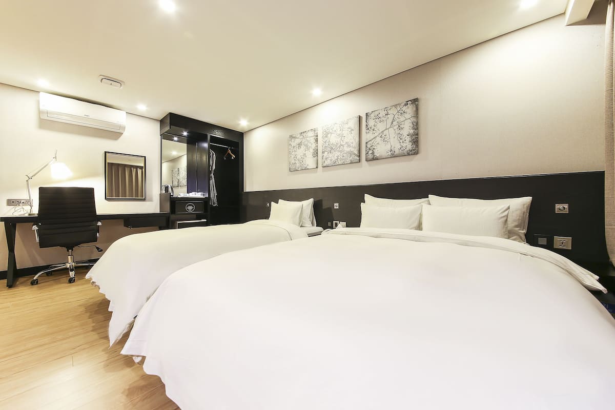 Ein Hotelzimmer mit zwei Betten, einem Schreibtisch, einem Stuhl und einem Spiegel.