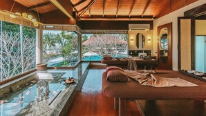 A spa room with a massage table, a glass table with a water feature, and a view of a pool and palm trees. - Sea Sand Sun Resort and Villas (Sattahip)