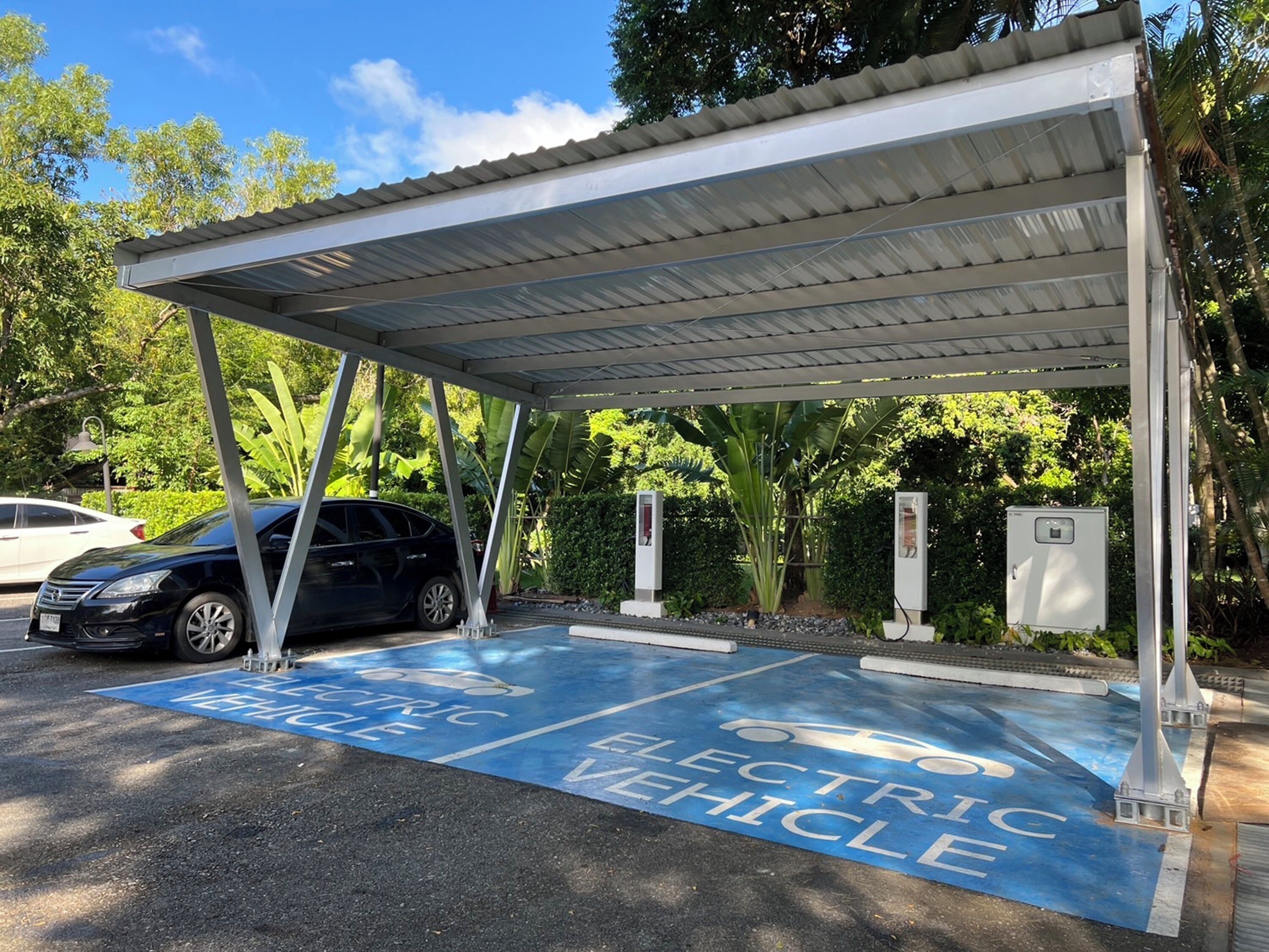 An electric vehicle charging station with a covered canopy, surrounded by greenery.