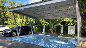 An electric vehicle charging station with a covered canopy, surrounded by greenery.