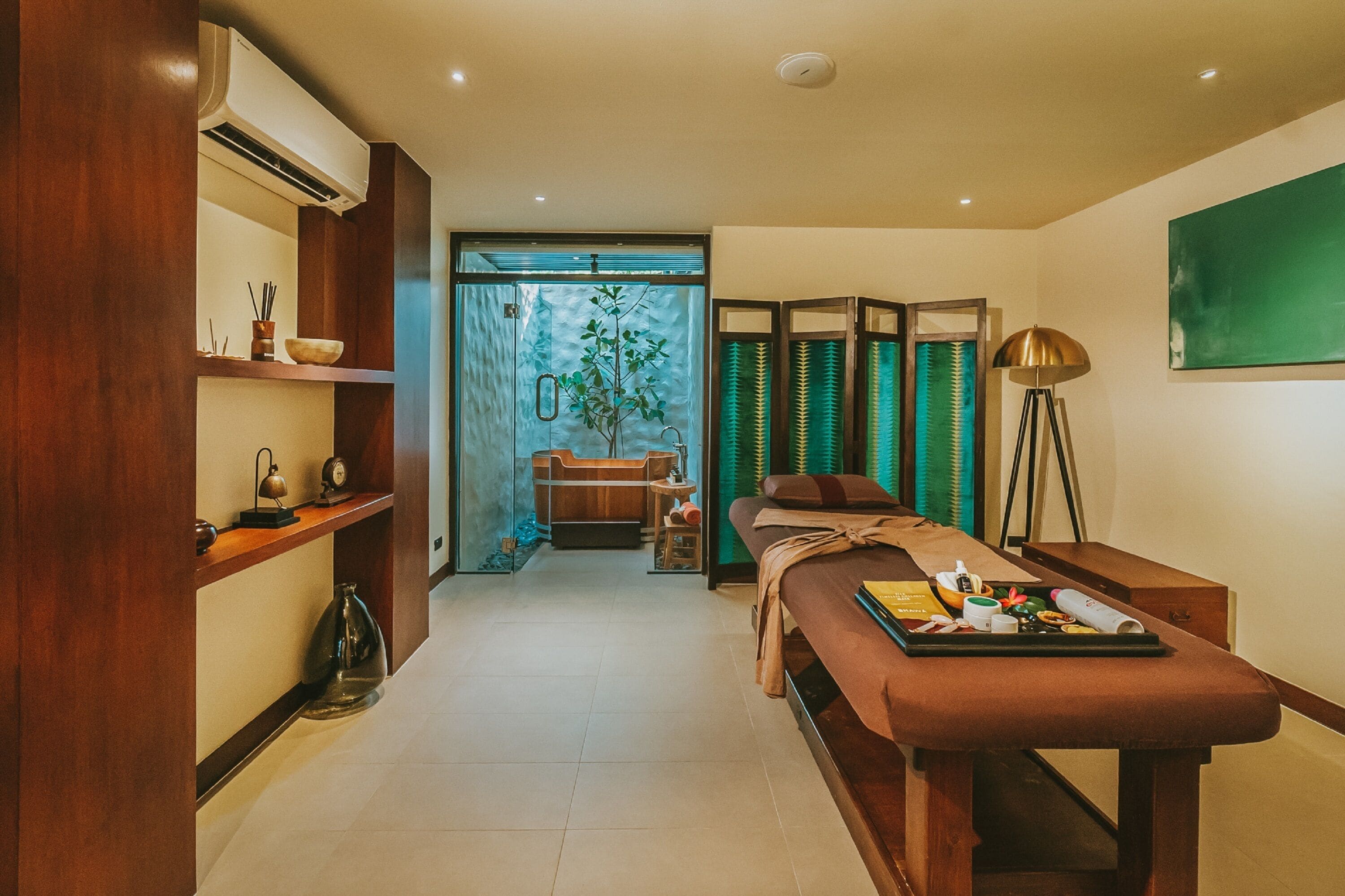A modern spa room with a massage table, a small seating area, and a large window with curtains.
