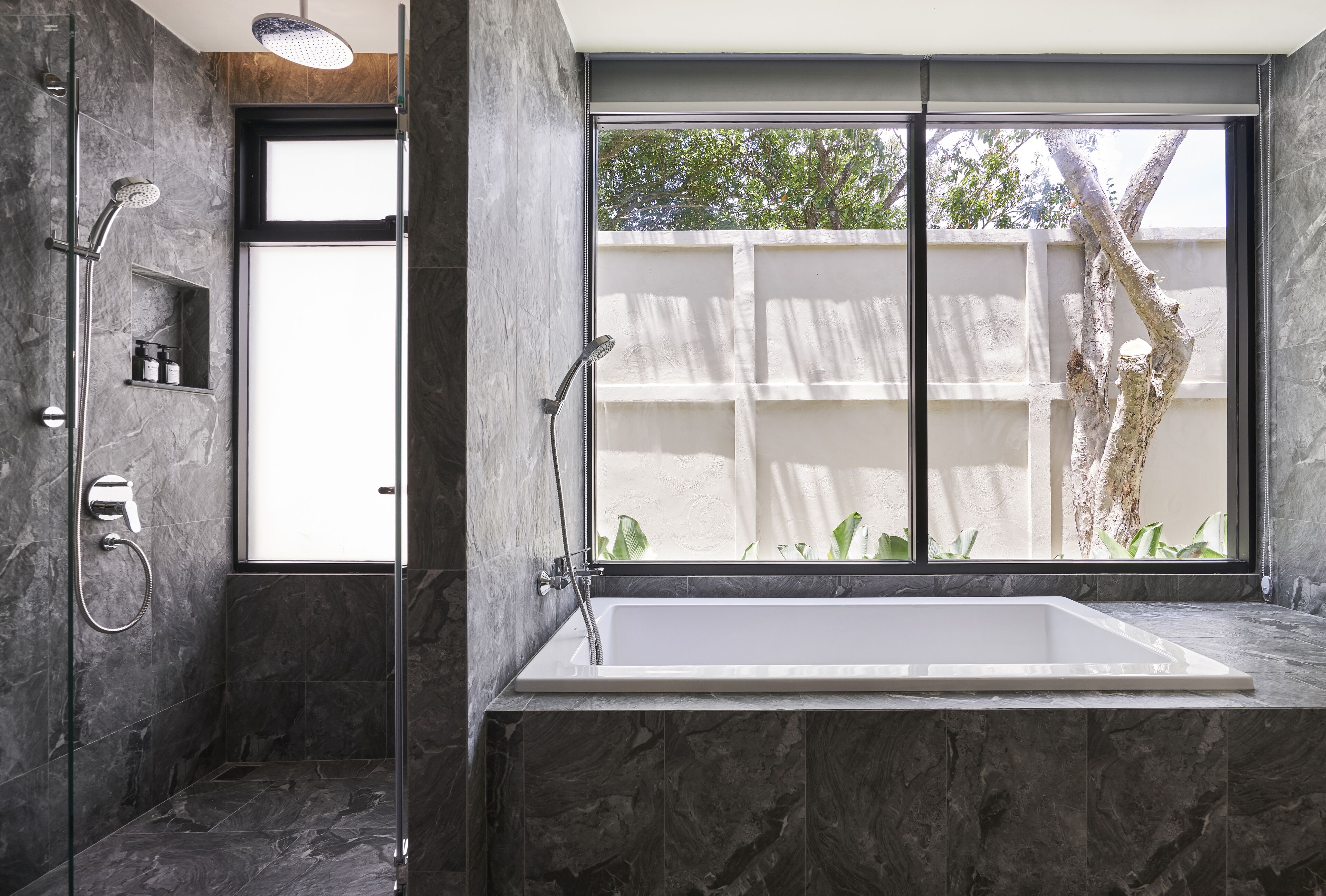 Un bagno moderno con una grande vasca, una doccia vetrata e vista su un albero.