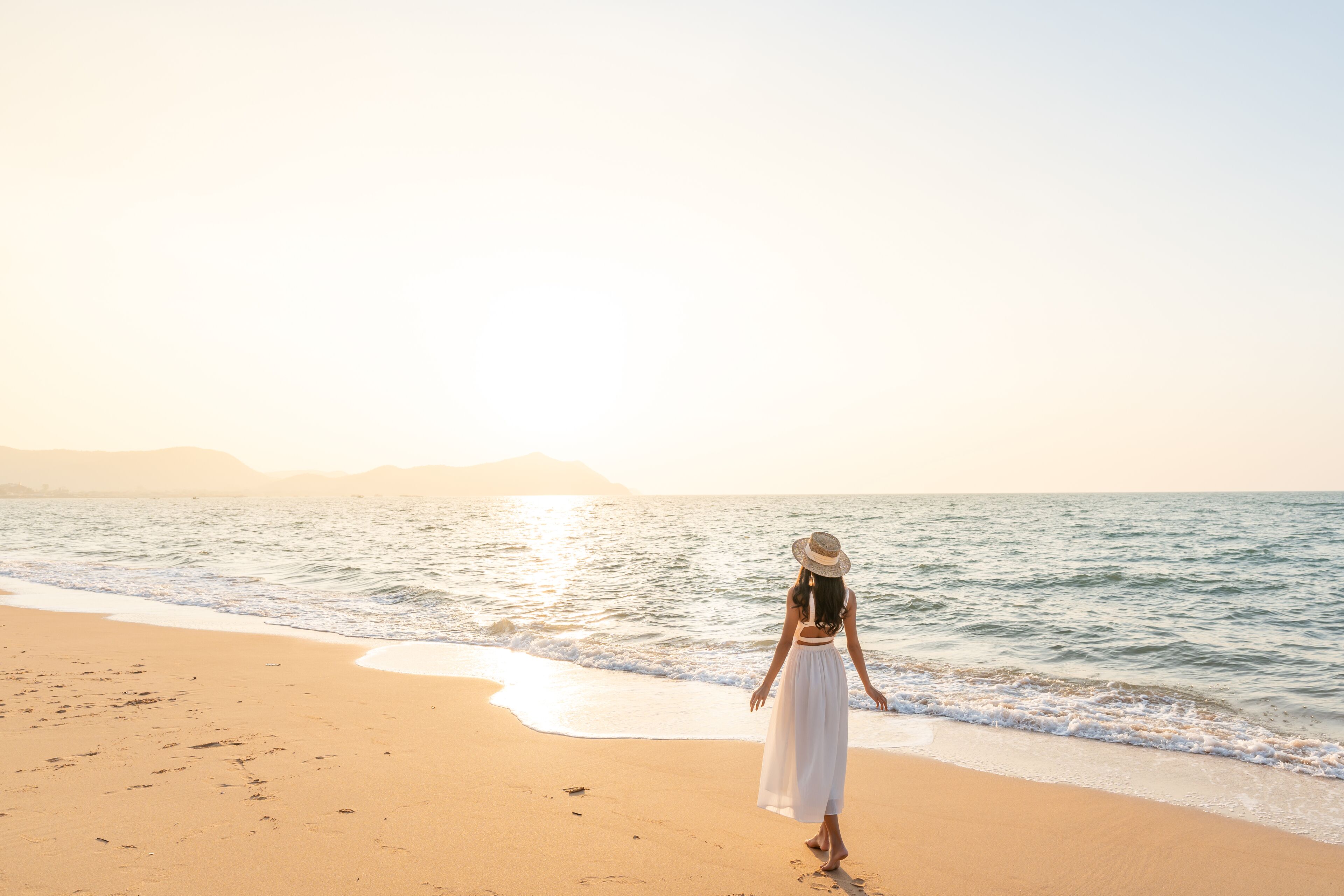 Una mujer caminando en una playa, con el océano al fondo.